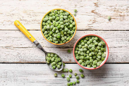 Bowls and spoon with frozen green peas on light wooden backgroundの写真素材