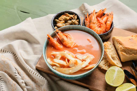 Bowl of tasty Cacciucco soup and ingredients on color wooden background