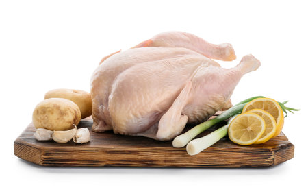 Board with whole raw chicken, lemon and vegetables on white backgroundの写真素材