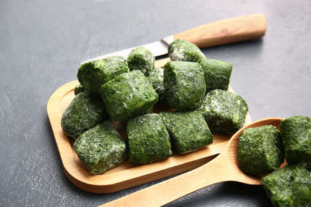 Board and spoon with frozen spinach on dark background