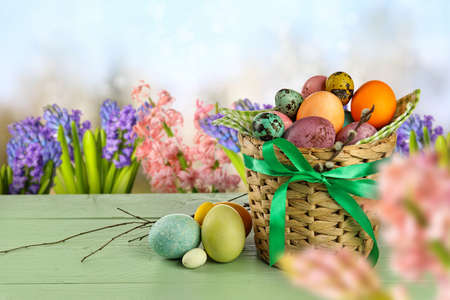 Wicker basket with painted Easter eggs on table in spring garden