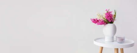 Vase with hyacinth flowers and candle on table against light background with space for text