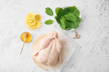 Board with whole raw chicken, lemon, spinach and honey on light backgroundの写真素材