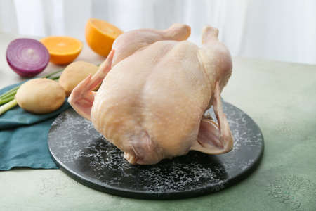 Board with whole raw chicken and vegetables on table, closeupの写真素材