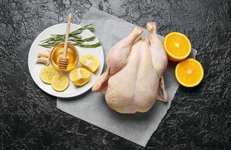 Parchment with whole raw chicken, orange, lemon and spices on dark backgroundの写真素材