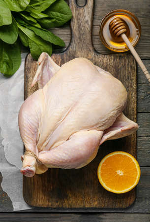 Board with whole raw chicken, orange and honey on wooden backgroundの写真素材