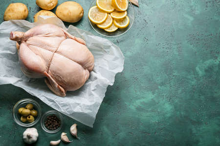 Parchment with whole raw chicken, lemon, vegetables and spices on color backgroundの写真素材