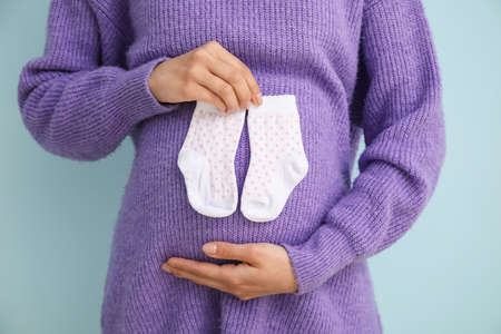 Pregnant woman with baby socks on color backgroundの写真素材