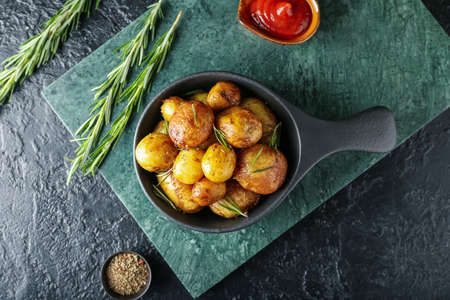 Frying pan with baked potatoes and rosemary on dark backgroundの写真素材