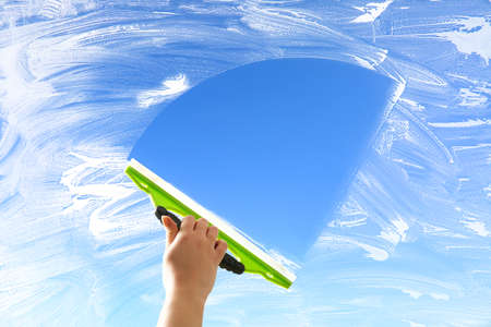 Washing of window with detergent and squeegee against blue sky