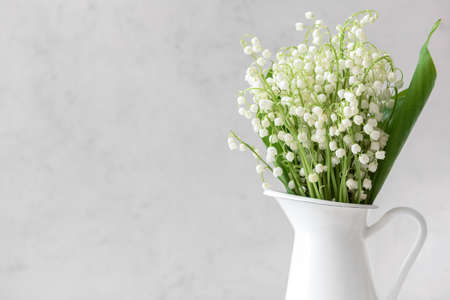 Jug with beautiful lily-of-the-valley flowers on light background