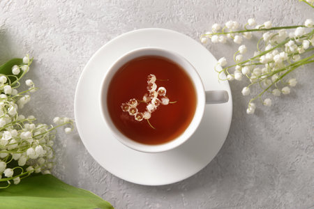 Beautiful lily-of-the-valley flowers and cup of tea on light background