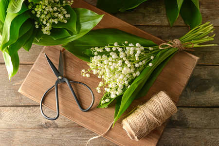 Beautiful lily-of-the-valley flowers, rope and scissors on wooden background