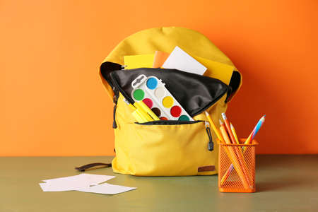 School backpack and stationery on color background