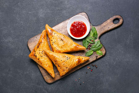 Board with tasty Uzbek samsa and tomato sauce on dark backgroundの写真素材
