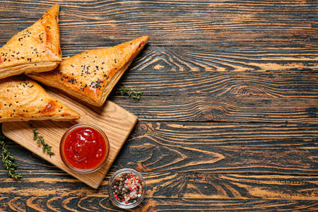 Board with tasty Uzbek samsa and tomato sauce on wooden backgroundの写真素材