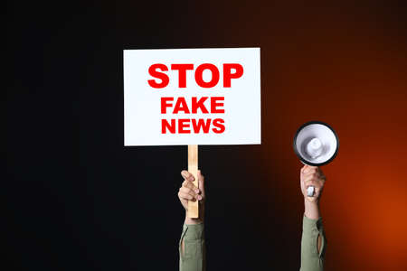 Woman holding megaphone and placard with text STOP FAKE NEWS on dark backgroundの写真素材