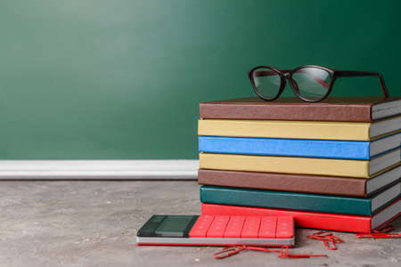 Stack of books, calculator, eyeglasses and paper clips on table in classroomの写真素材