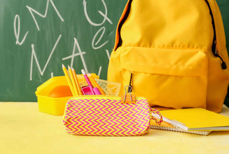 Pencil case with stationery and backpack on table in classroom