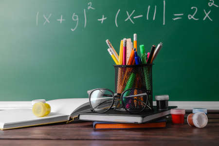 Set of stationery with paints and eyeglasses on table in classroomの写真素材
