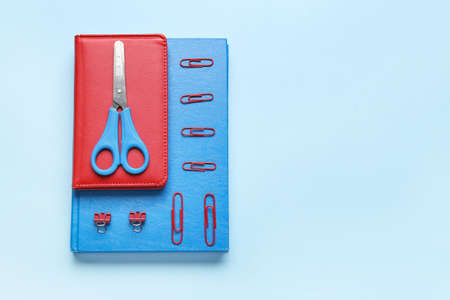 Notebooks, scissors and clips on color background