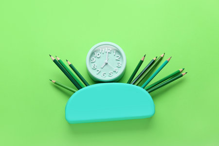 Case with color pencils and alarm clock on green backgroundの写真素材
