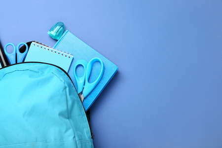 Backpack with stationery on blue background, closeup