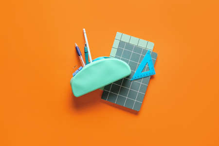Pencil case with stationery and notebooks on color background