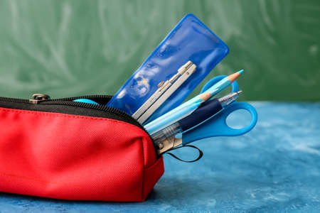 Red pencil case with stationery on color background, closeup