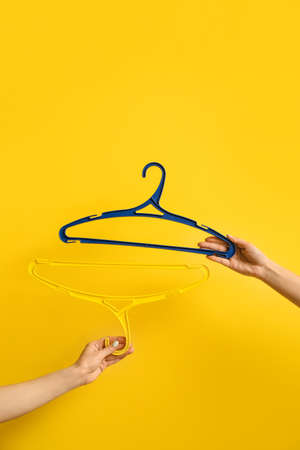 Female hands with clothes hangers on color background