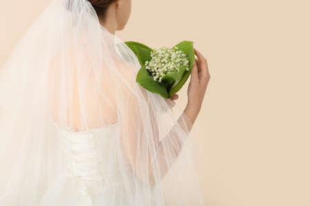 Bride with bouquet of beautiful lily-of-the-valley flowers on light backgroundの写真素材