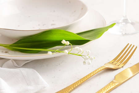 Beautiful table setting with lily-of-the-valley flowers on light background