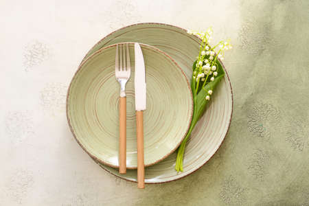 Beautiful table setting with lily-of-the-valley flowers on light background