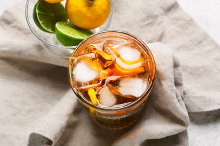 Glass of tasty ice tea with citrus fruits on light background