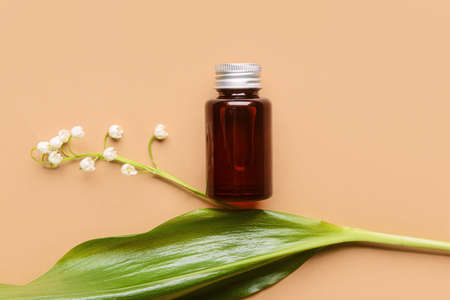 Bottle with essential oil and lily-of-the-valley flower on color backgroundの写真素材