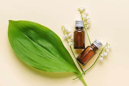 Bottles with essential oil and lily-of-the-valley flowers on color backgroundの写真素材