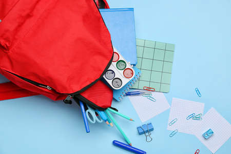 Red backpack with stationery on color background, closeup