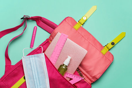 School backpack, stationery, medical mask and sanitizer on color background, closeup