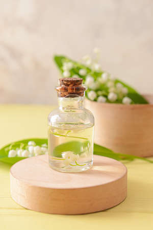Bottle with essential oil and lily-of-the-valley flowers on color wooden backgroundの写真素材