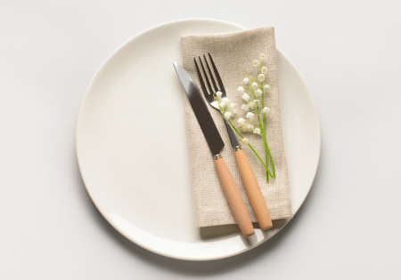 Beautiful table setting with lily-of-the-valley flowers on light background