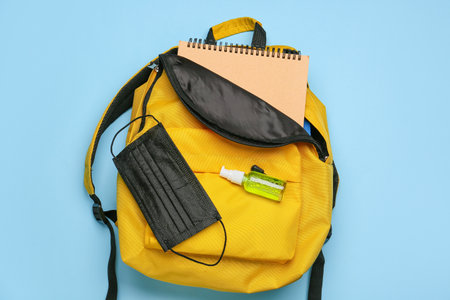 Stylish backpack with notebook, medical mask and sanitizer on color backgroundの写真素材