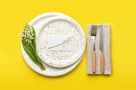 Beautiful table setting with lily-of-the-valley flowers on color background