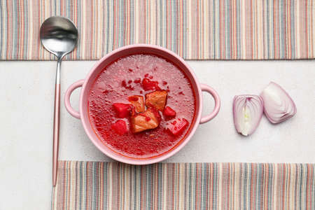 Pot with tasty borscht, onion and spoon on light backgroundの写真素材
