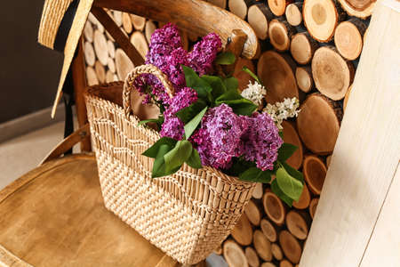 Bag with lilac flowers on chair near wooden wallの写真素材