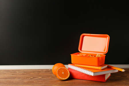 Lunch box with food, oranges and stationery on wooden table in classroomの写真素材