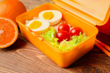 Lunch box with food and oranges on wooden background, closeup