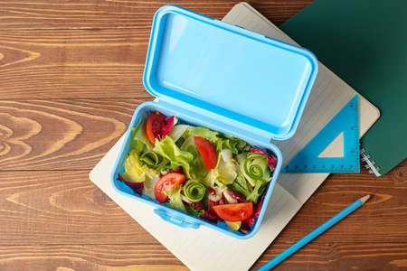 Lunch box with tasty food and stationery on wooden background