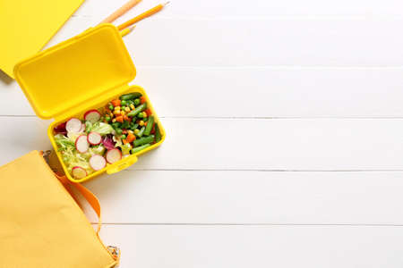 Lunch box with vegetables, bag and stationery on light wooden backgroundの写真素材