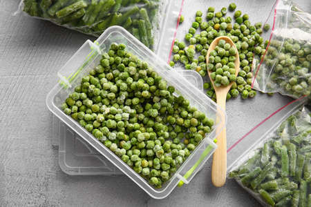 Plastic container and bags with different frozen vegetables on gray background