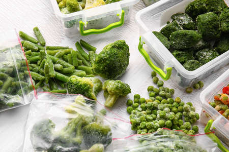 Plastic containers and bags with different frozen vegetables on light backgroundの写真素材